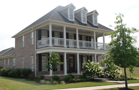 Replacement windows installed in a large brick two-story home with front porch and balcony, large white columns, and 3 dormers.