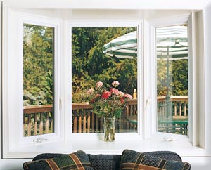Interior view of white bay windows with a vase of flowers in front.