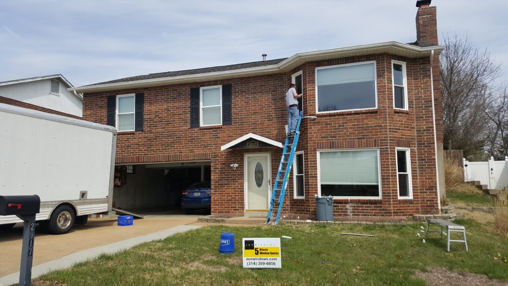 Man standing on ladder measuring top window of brick home