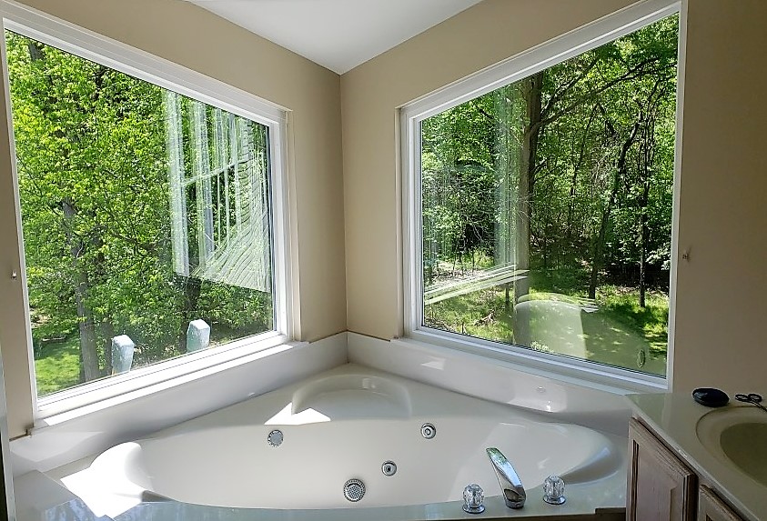Double-pane picture windows over a jacuzzi in a bathroom. View of trees outside.