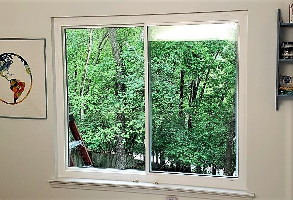 Close-up of a slider window with a view of trees outdoors. White wall around window.