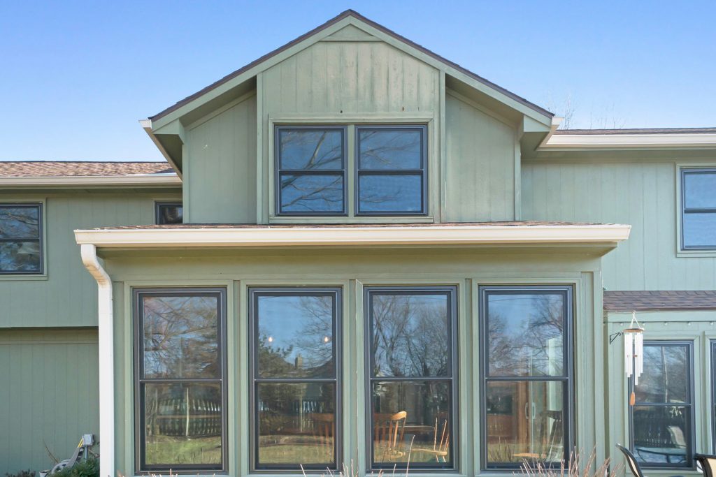 A row of fiberglass windows on the back side of a home with green vertical siding.