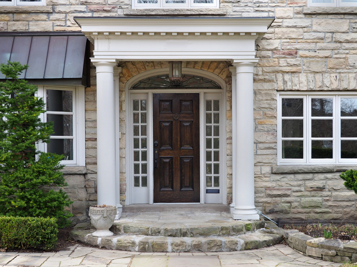 Dark woodgrain paneled front entry door with surrounding white windows in a white/tan stone home.